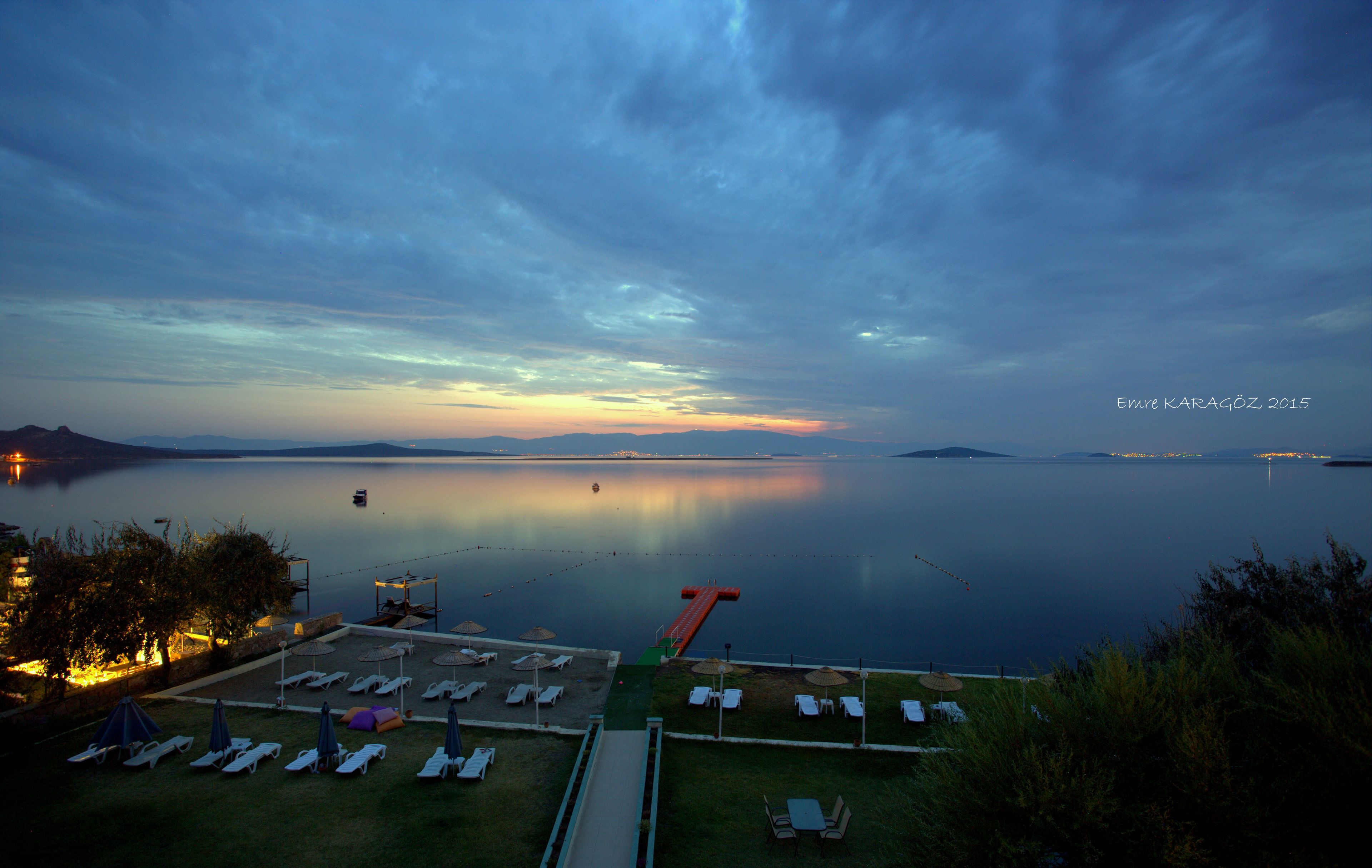 A calm waterfront view with lounge chairs and umbrellas, a slide, and a clear sky.