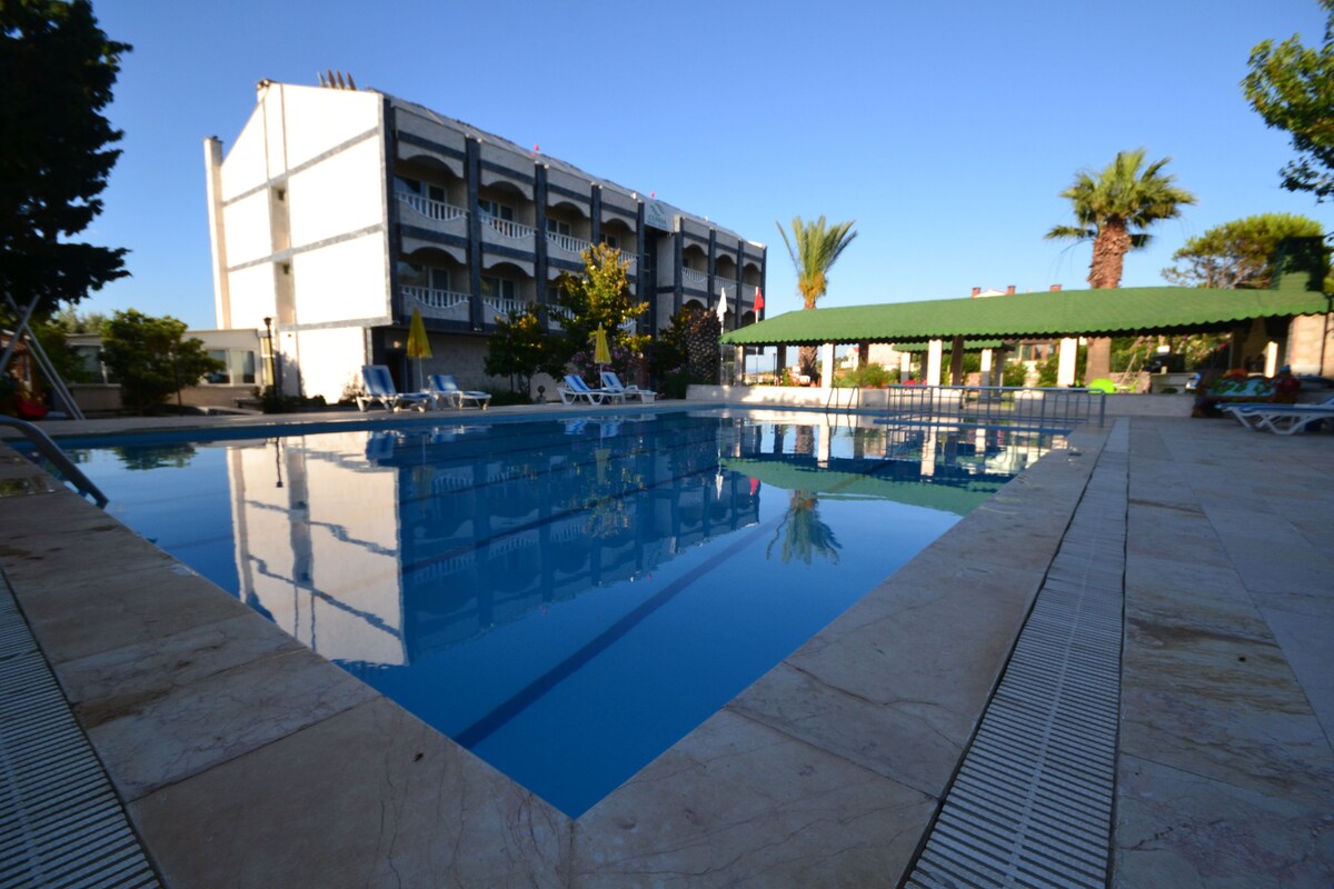 A swimming pool with lounge chairs, a building with balconies, and palm trees.