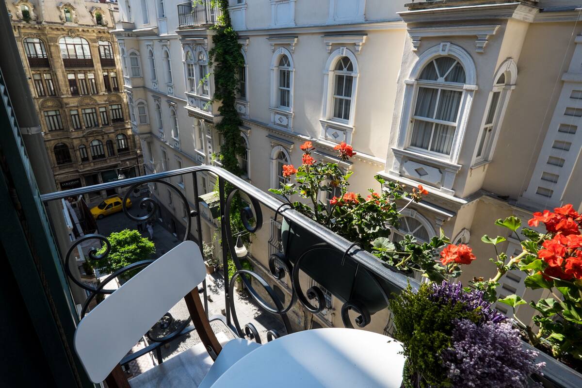 A balcony with a white chair, a railing, and potted plants with red and purple flowers.