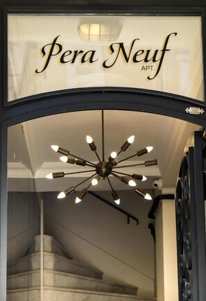 Ein Eingangsbereich mit einem Schild, das "Pera Neub APT." zeigt, und einer modernen Deckenleuchte.