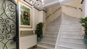 A staircase with a marble finish, a white wall with a framed portrait, and a black metal door with a decorative design. - Pera Neuf (Istanbul)