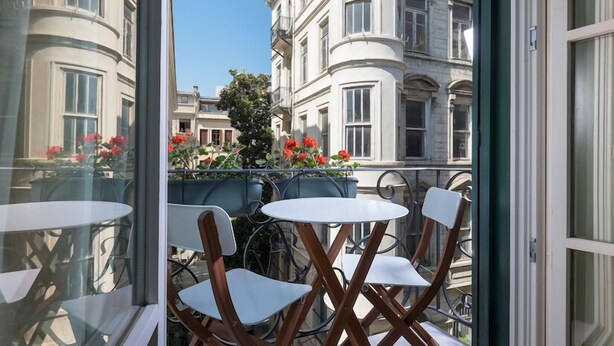 A balcony with white chairs and a table, overlooking a street with buildings and red flowers. - Pera Neuf (Istanbul)