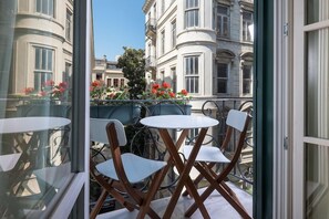 A balcony with white chairs and a table, overlooking a street with buildings and red flowers. - Pera Neuf (Istanbul)