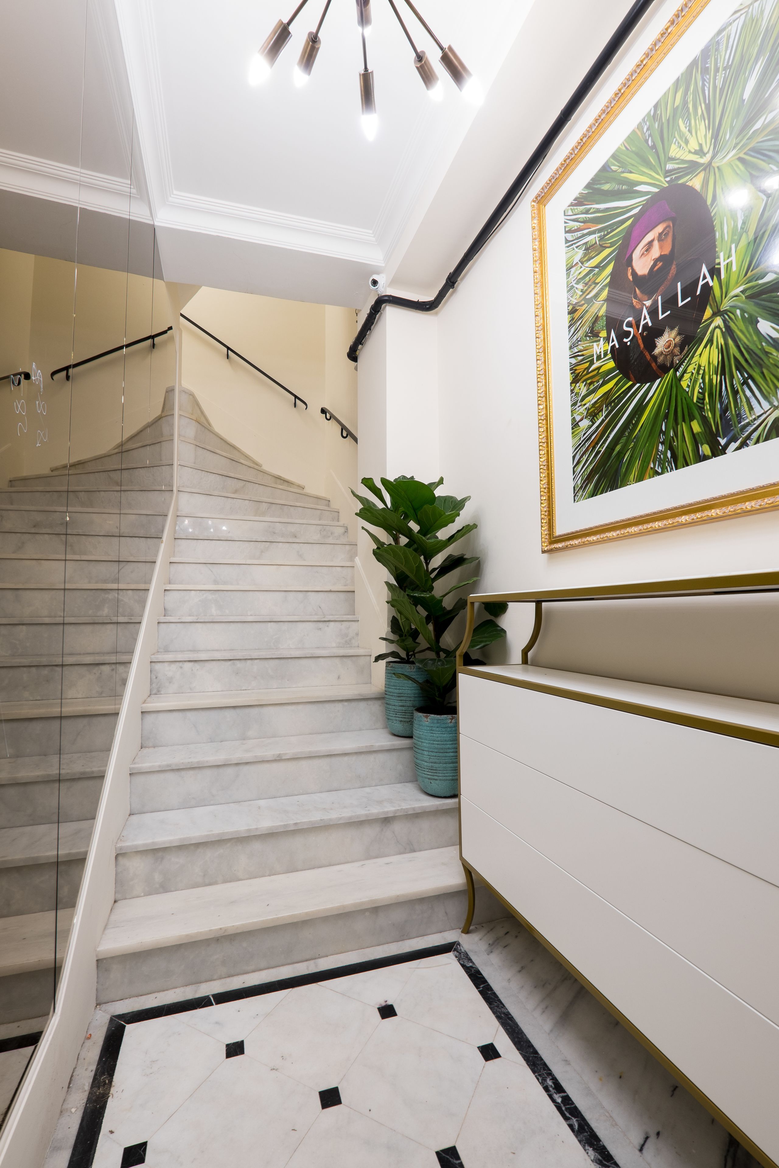Uma escadaria com degraus de mármore, uma parede branca com um quadro emoldurado e um vaso com planta.