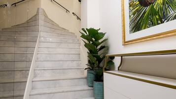 Uma escadaria com degraus de mármore, uma parede branca com um quadro emoldurado e um vaso com planta.