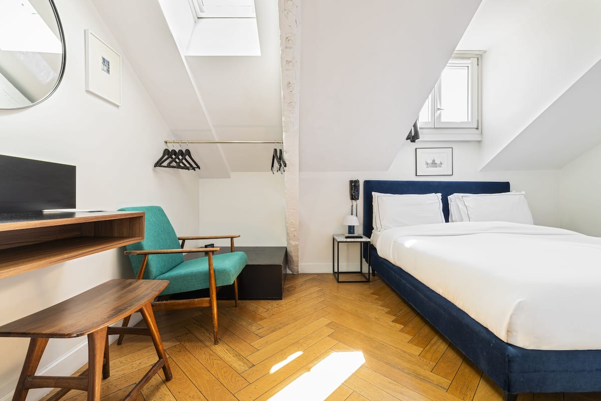 A room with a bed, a desk, a chair, a small table, and a window.