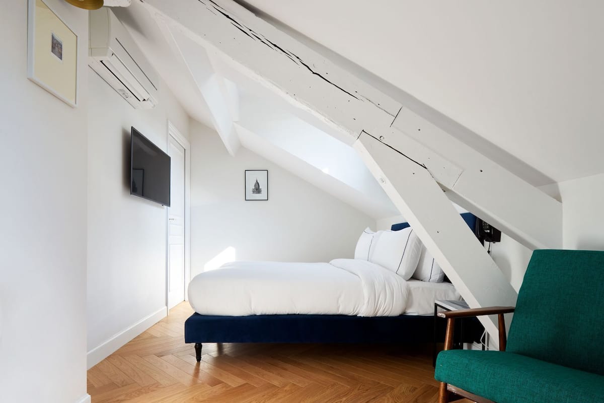 A bedroom with a sloped ceiling, a bed, a chair, and a framed picture on the wall.