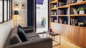 A living room with a sofa, a coffee table, a bookshelf, and a window with curtains. - Hôtel Rendez-vous Batignolles (Paris)