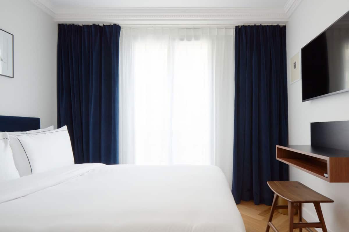 A hotel room with a large bed, a desk, a television, and a window with curtains.