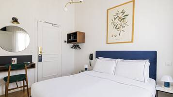 Habitación de hotel con cama, escritorio con silla, teléfono, estante en la pared, impresión botánica enmarco y espejo.