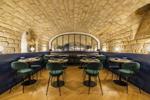 A restaurant with stone walls, wooden floors, and green upholstered chairs. - Hôtel Rendez-vous Batignolles (Paris)