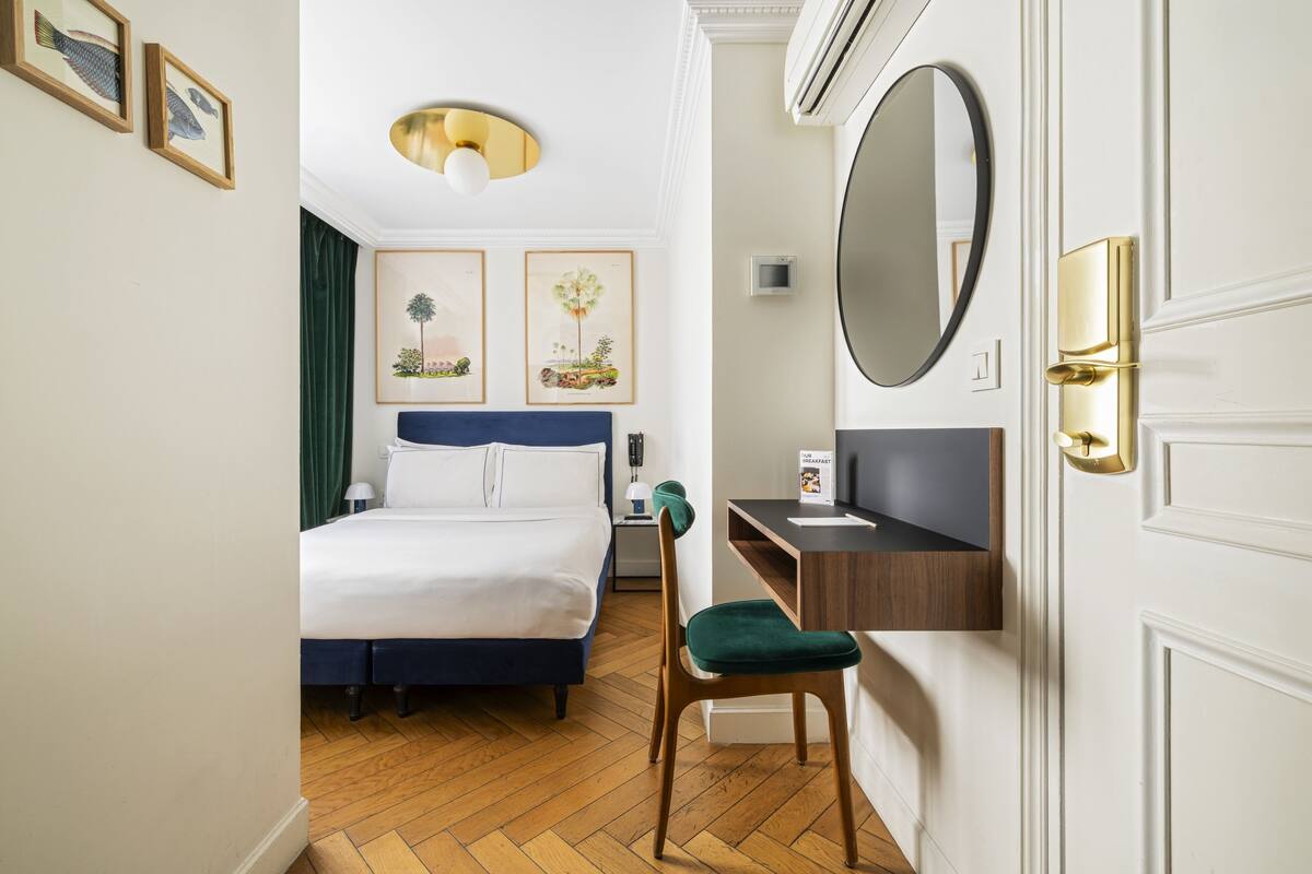 A hotel room with a bed, desk, chair, and a large mirror.
