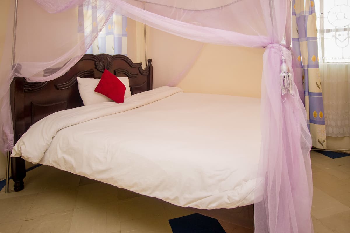 A bed with a canopy, a red pillow, and a wooden headboard.
