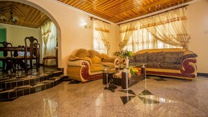 A living room with a wooden ceiling, a patterned sofa, a coffee table, and a dining area with chairs and a table. - Nairobi Airport Rest House (Nairobi)