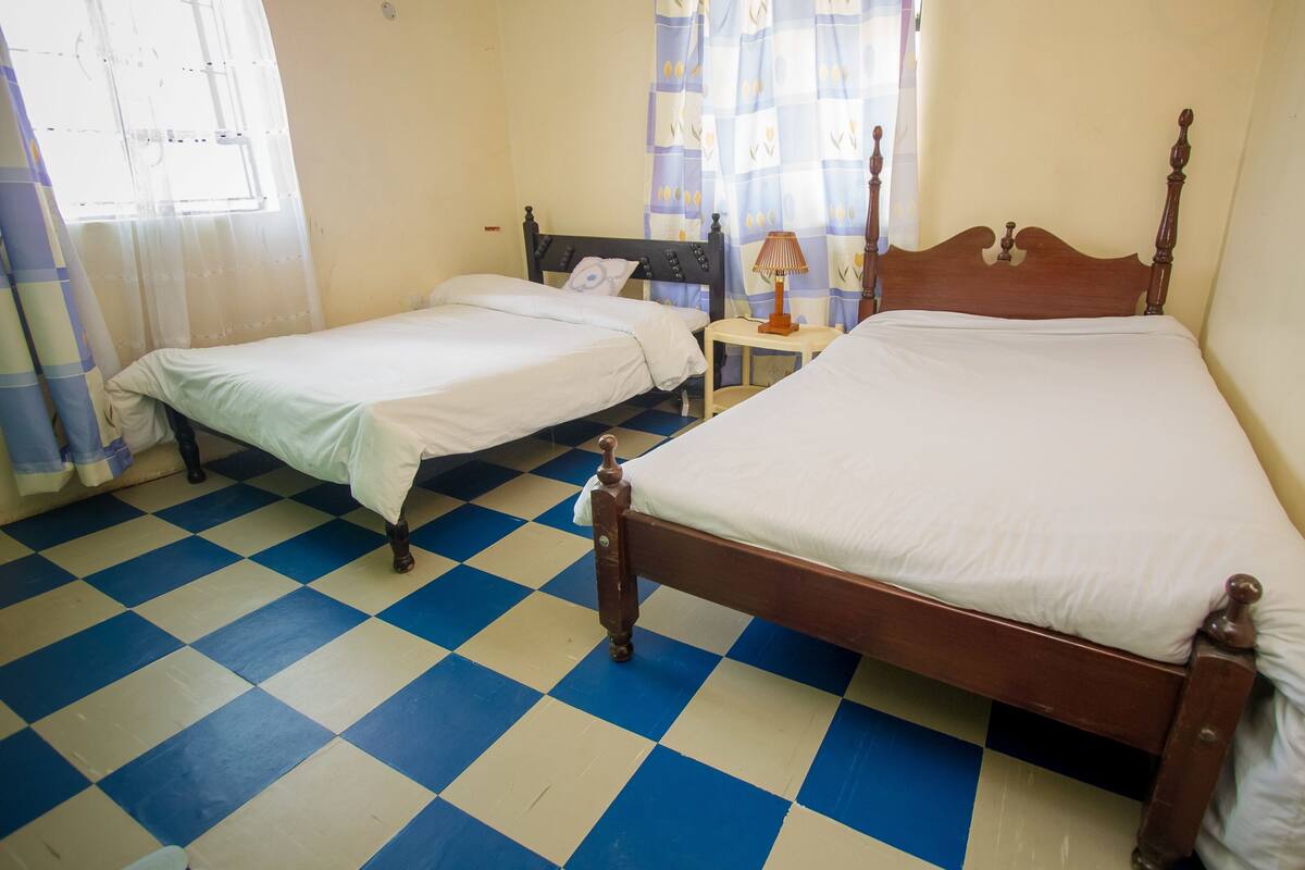 A room with two beds, a checkered floor, and a window with curtains.