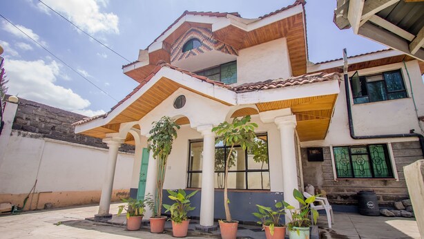 A two-story house with a tiled roof, a porch with columns, and several potted plants. - Nairobi Airport Rest House (Nairobi)