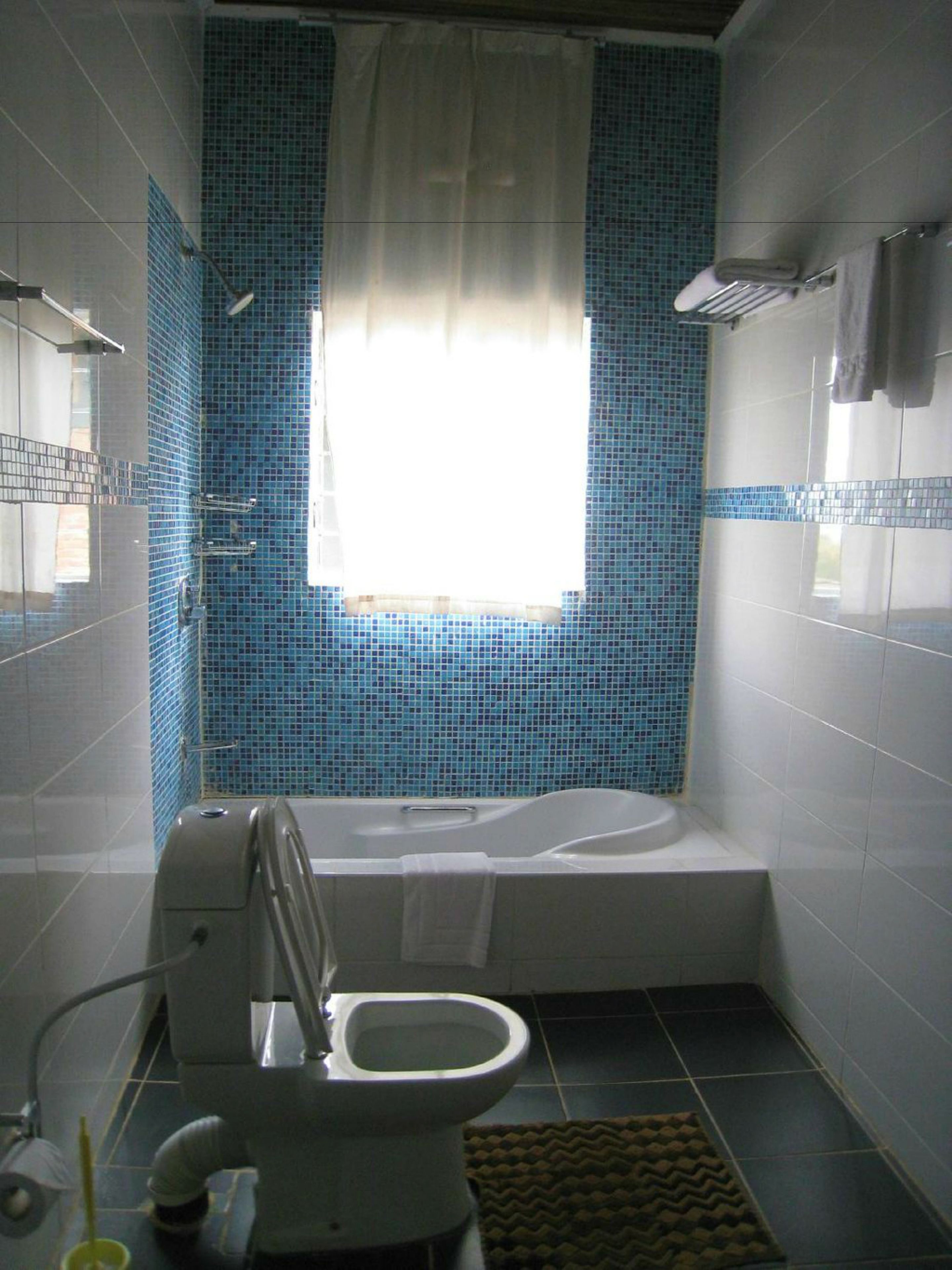 A bathroom with a bathtub, toilet, and a window with blue-tiled walls.