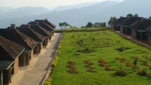 Una hilera de edificios tradicionales con un sendero que atraviesa un campo verde, rodeado de montañas.