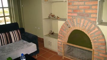 A living room with a brick fireplace, a sofa, a coffee table, and a small shelf with decorative items.