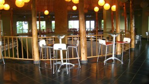Un espacio interior amplio con techos altos, pilares de bambú y una zona de bar central con sillas y mesas.