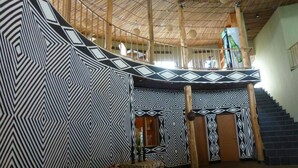 Un interior espacioso con techo alto, paredes de diseño geométrico, una escalera y una zona de estar con sofá.