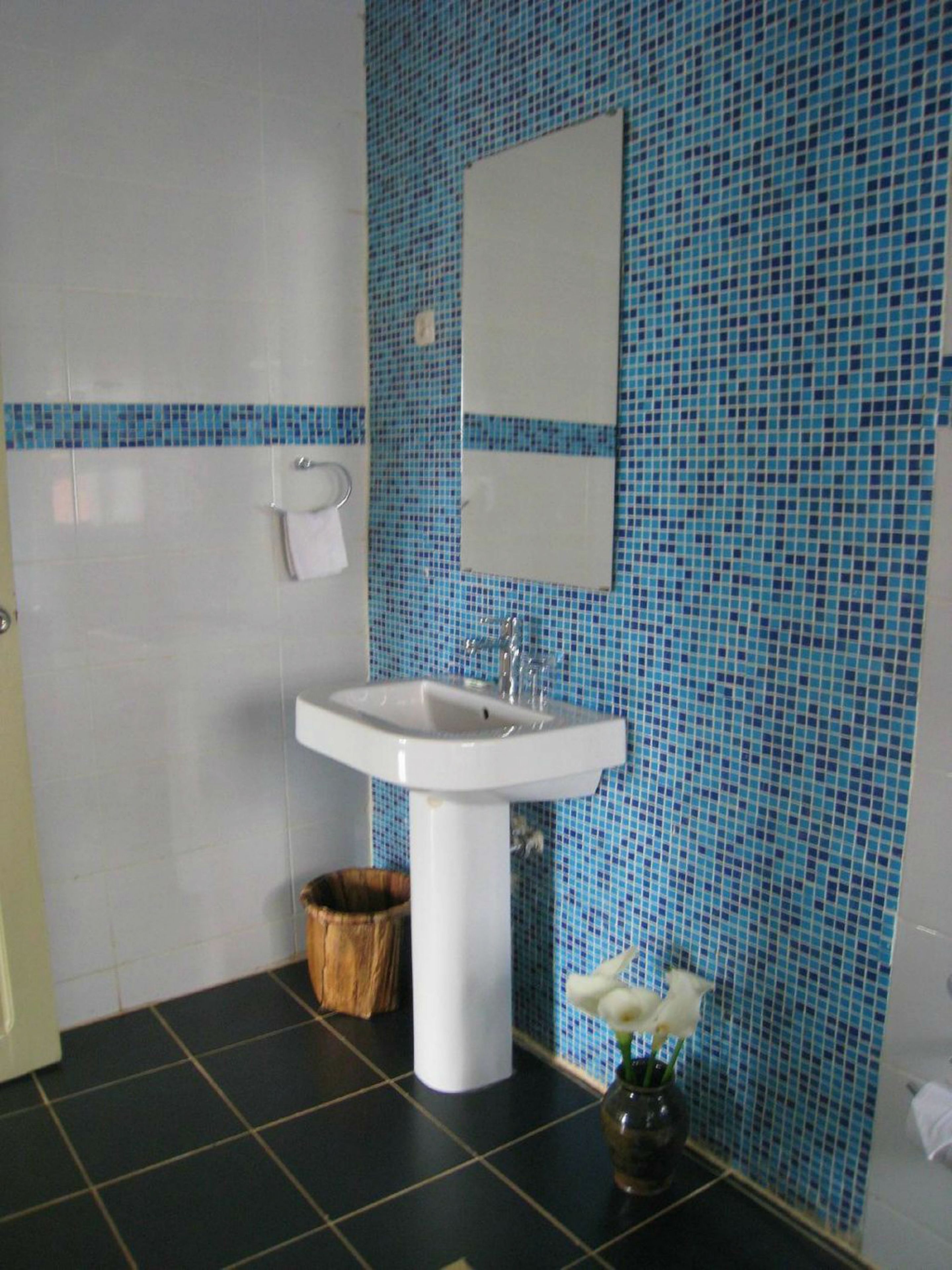 A bathroom with a white sink, blue mosaic tiles, a wooden basket, and a vase with white flowers.