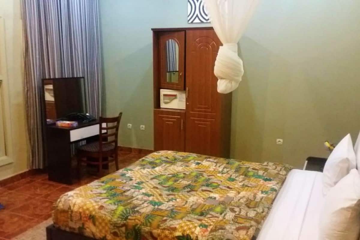 A bedroom with a bed, a desk, a chair, a wardrobe, and a mosquito net.
