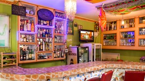 A bar area with a tiled counter, red bar stools, and shelves stocked with bottles. - Ogalis K Coast Hotel (Mtwapa)