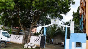 The entrance to Ogalas-K-Coast Hotel with a sign, a tree, and a truck parked nearby. - Ogalis K Coast Hotel (Mtwapa)