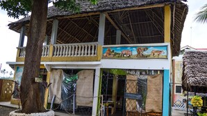 A two-story building with a balcony, a mural of animals, and a tree in front. - Ogalis K Coast Hotel (Mtwapa)