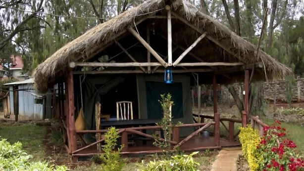 A rustic cabin with a thatched roof, a wooden deck, and a small porch area. - Oloolua Resort & Campground (Ngong)