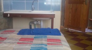 A bed with a striped blanket, a wooden door, and a bathroom with a sink and mirror.