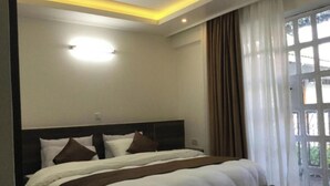 A bedroom with a large bed, a headboard, and a window with curtains. - Oriental Palace Hotel (Embu)