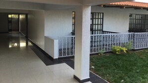A covered outdoor area with a tiled floor, a white railing, and a small garden. - Oriental Palace Hotel (Embu)