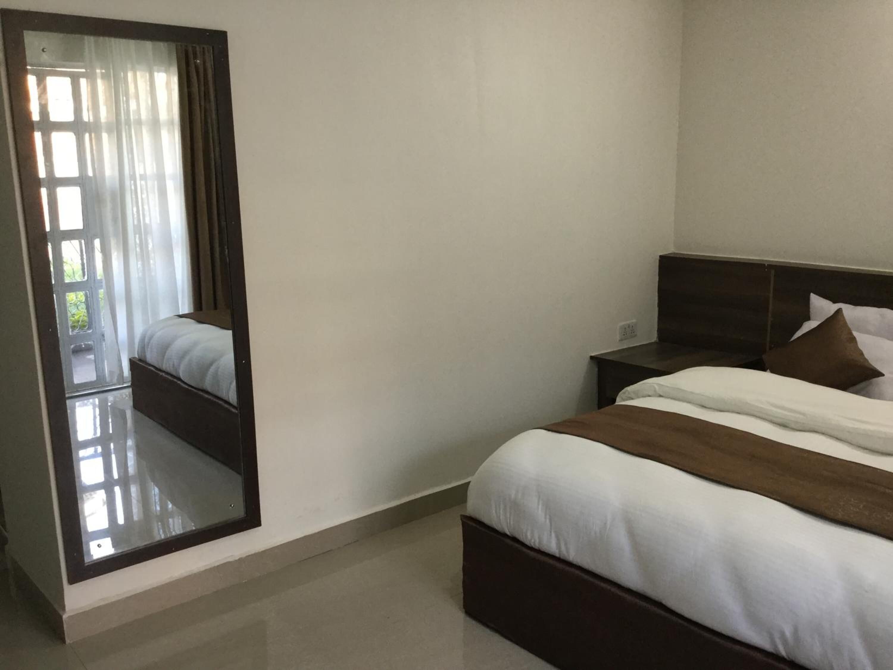 A bedroom with a large mirror, a bed with white and brown bedding, a nightstand, and a wooden headboard.