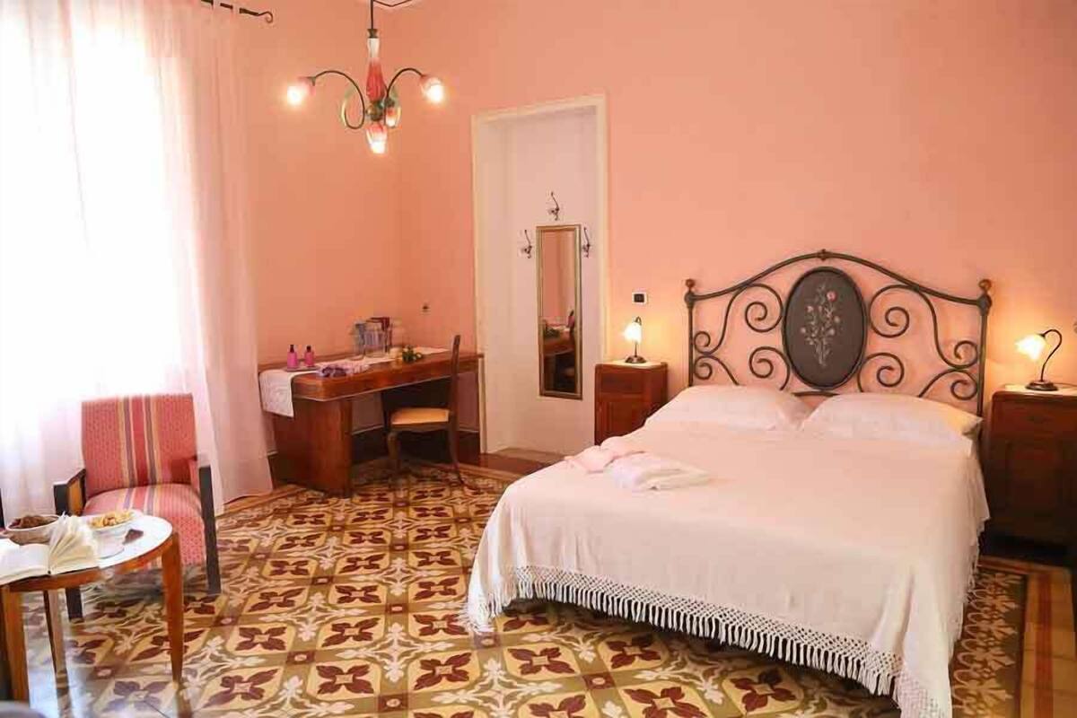 A bedroom with a bed, a desk, a chair, a mirror, and a chandelier.