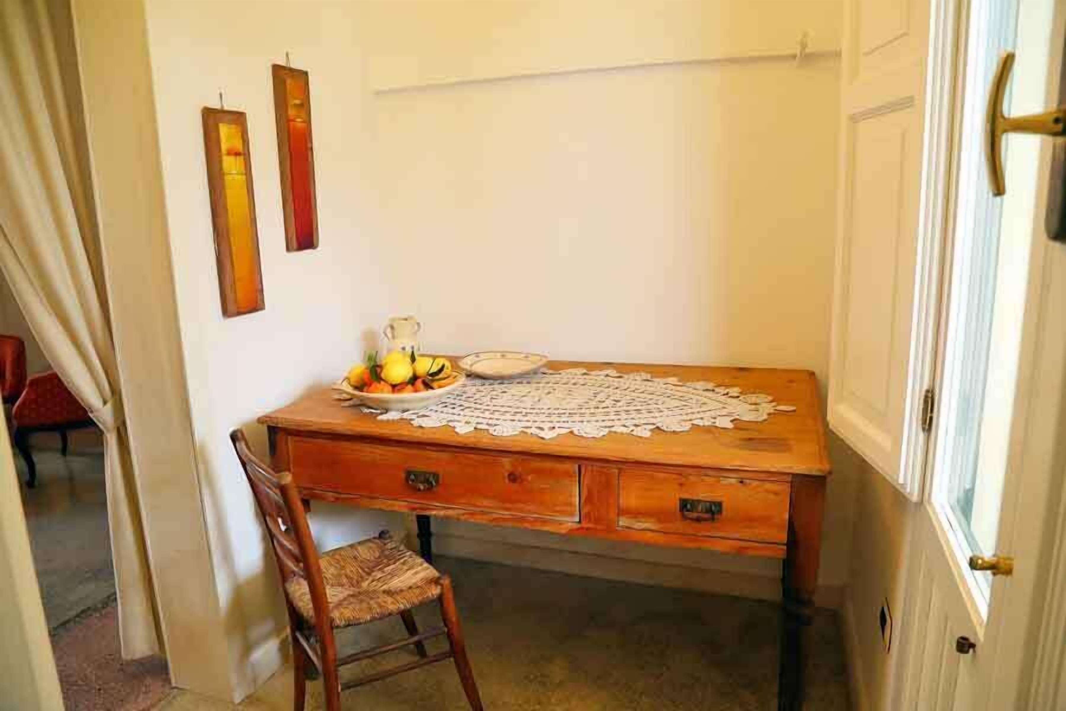 A wooden desk with a lace tablecloth, a chair, and a bowl of fruit.