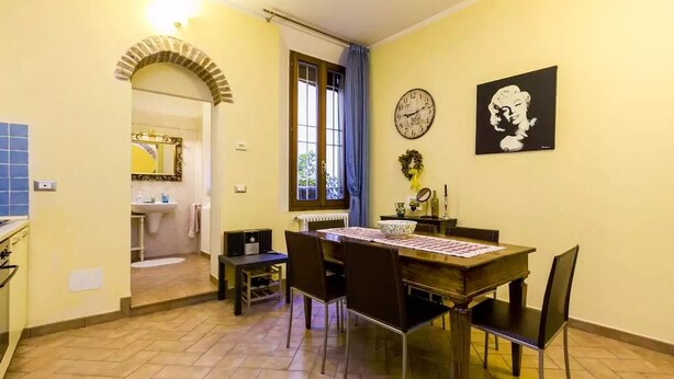 Un coin repas avec une table dressée pour quatre personnes, une horloge et une œuvre d’art encadrée accrochée au mur.