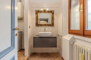 Un baño con un lavamanos blanco, un espejo grande con un marco ornamentado y una puerta de madera con un panel de vidrio.