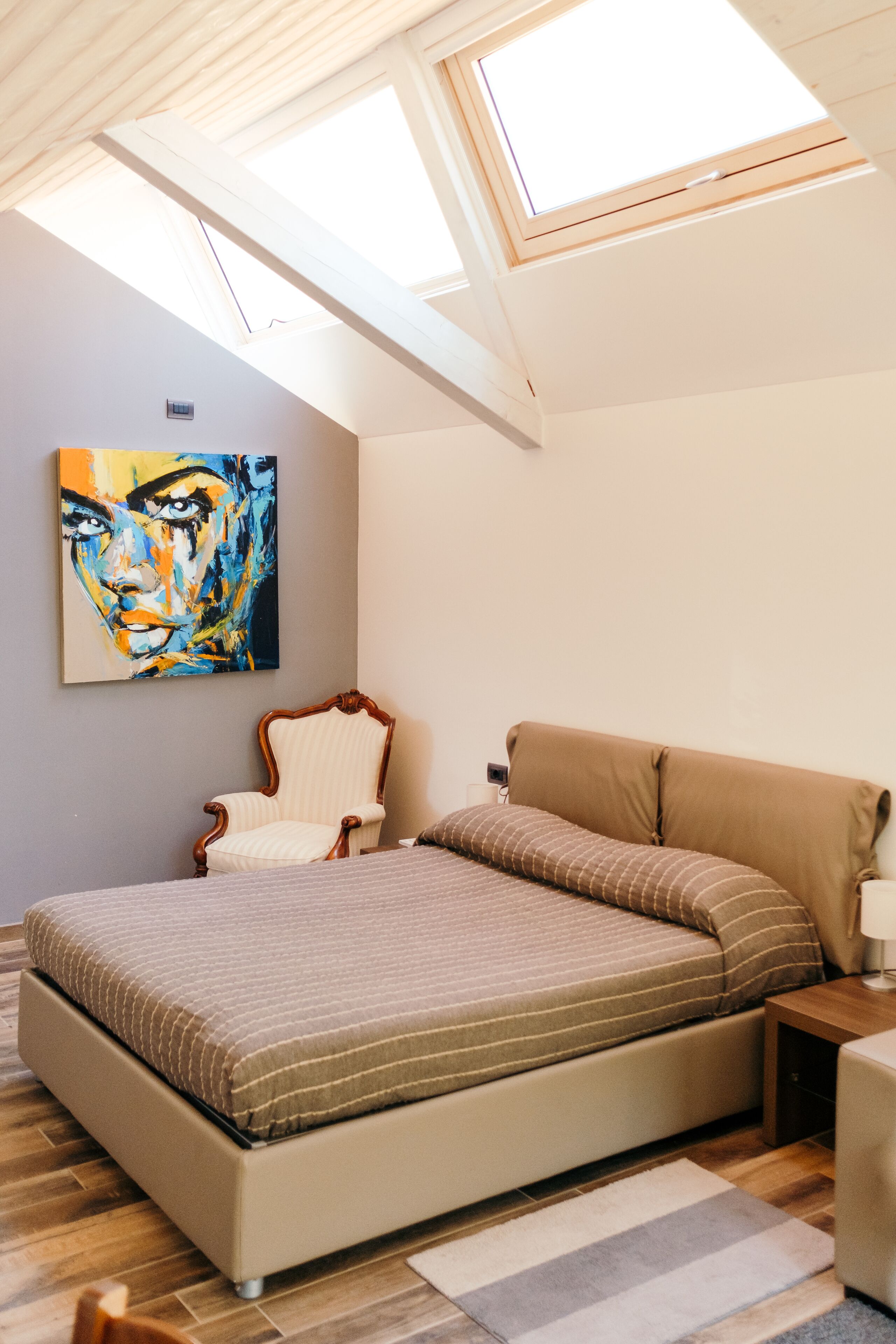 A bedroom with a bed, a chair, a painting, and skylights.