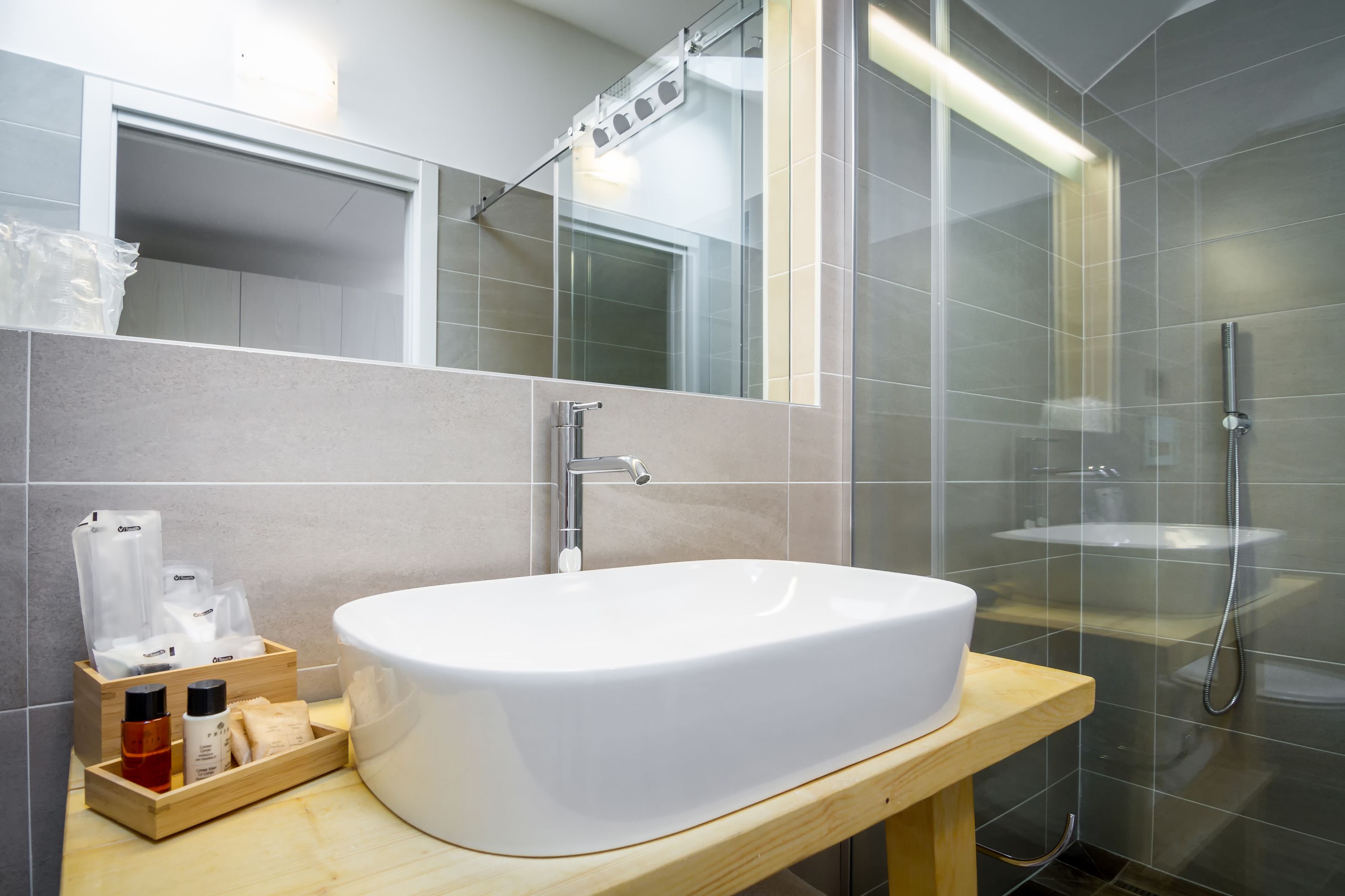 A modern bathroom with a large white sink, a wooden vanity, a glass shower enclosure, and a mirror above the sink.