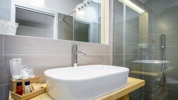 A modern bathroom with a large white sink, a wooden vanity, a glass shower enclosure, and a mirror above the sink.