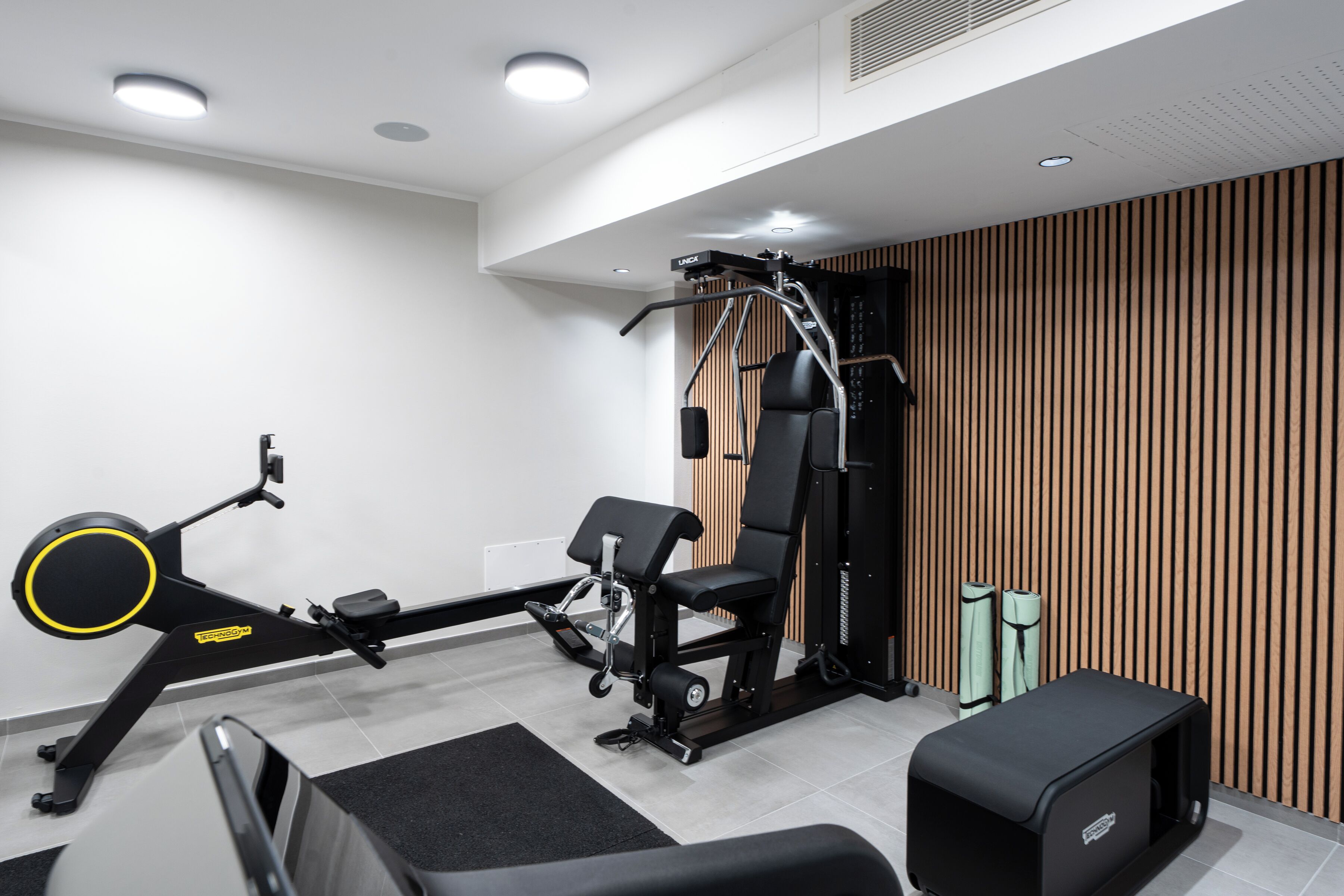 A modern gym with exercise equipment, a bench, and a wall-mounted rack.
