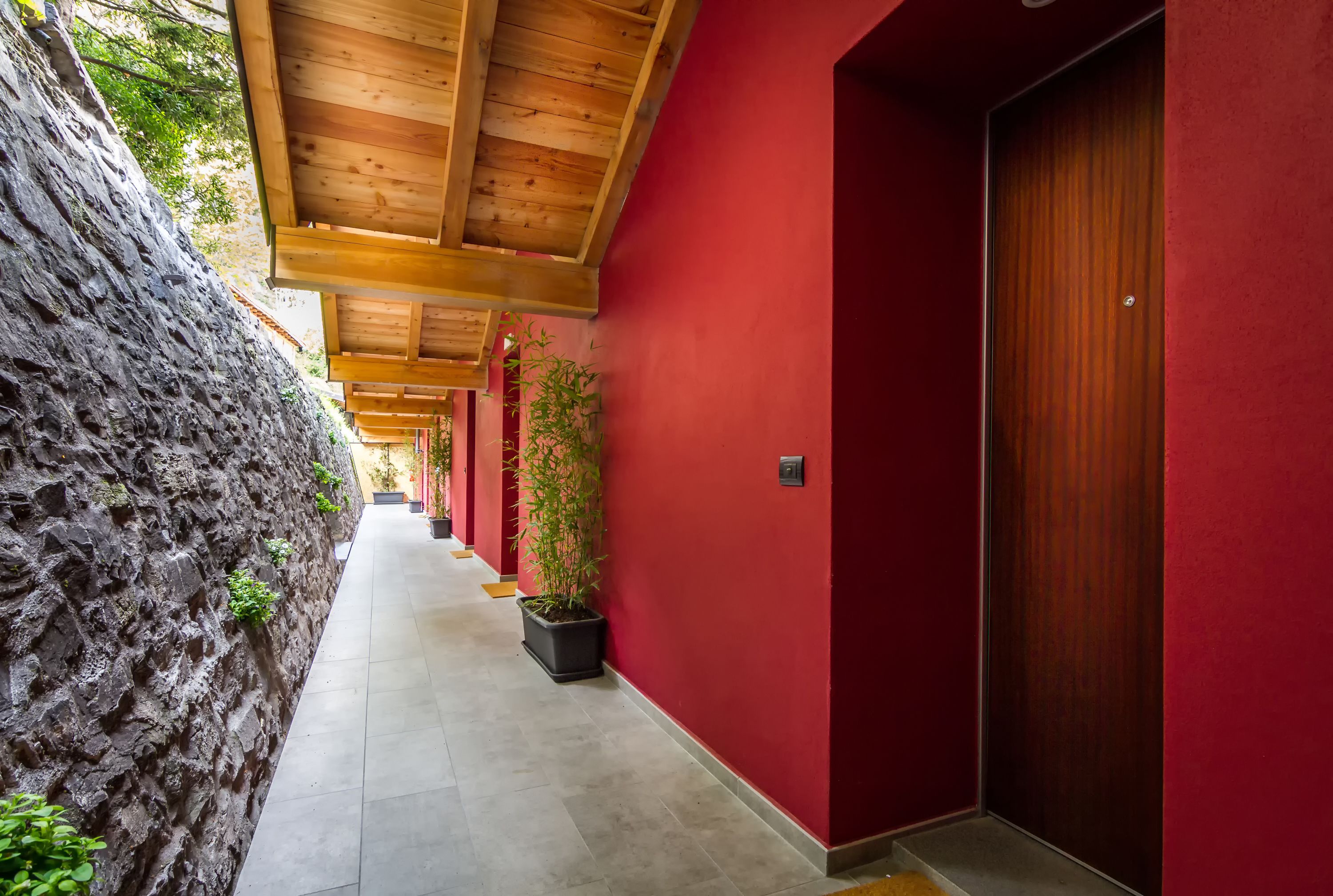 A corridor with red walls, wooden ceiling beams, and a stone wall on one side.