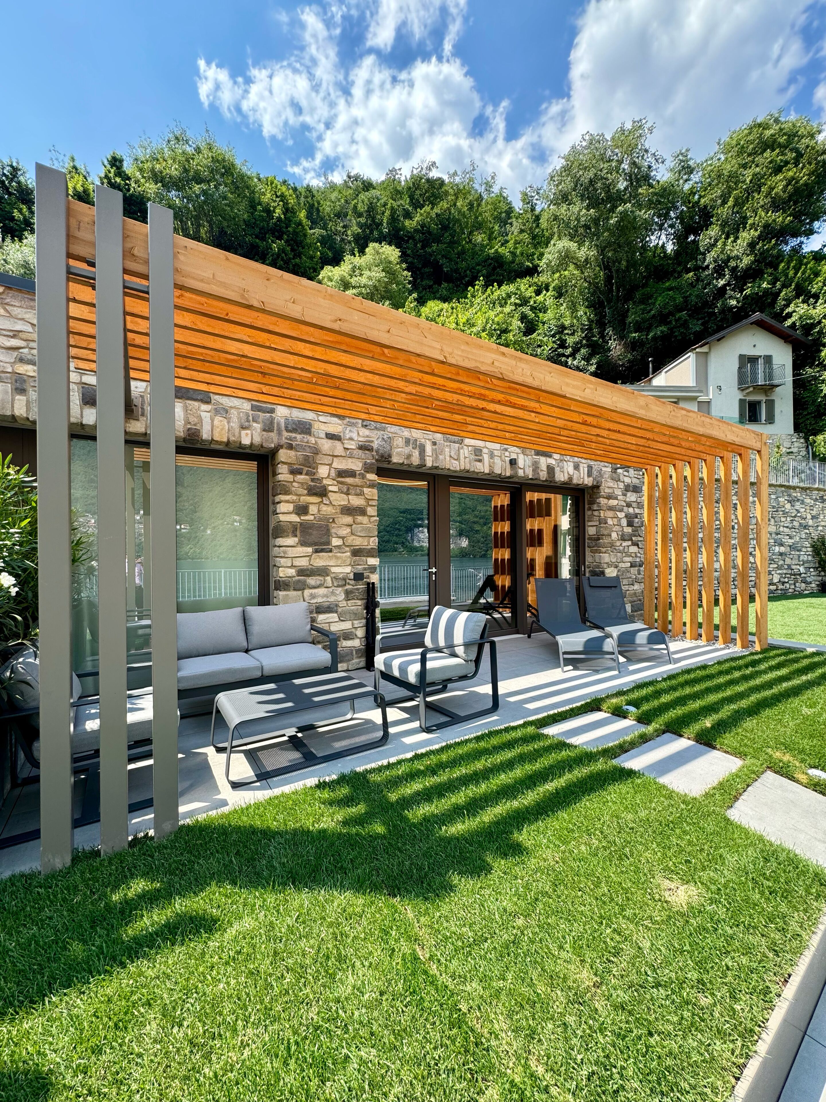 Een modern huis met een gevel van natuursteen, een schuin houten dak en een terras met tuinmeubilair.