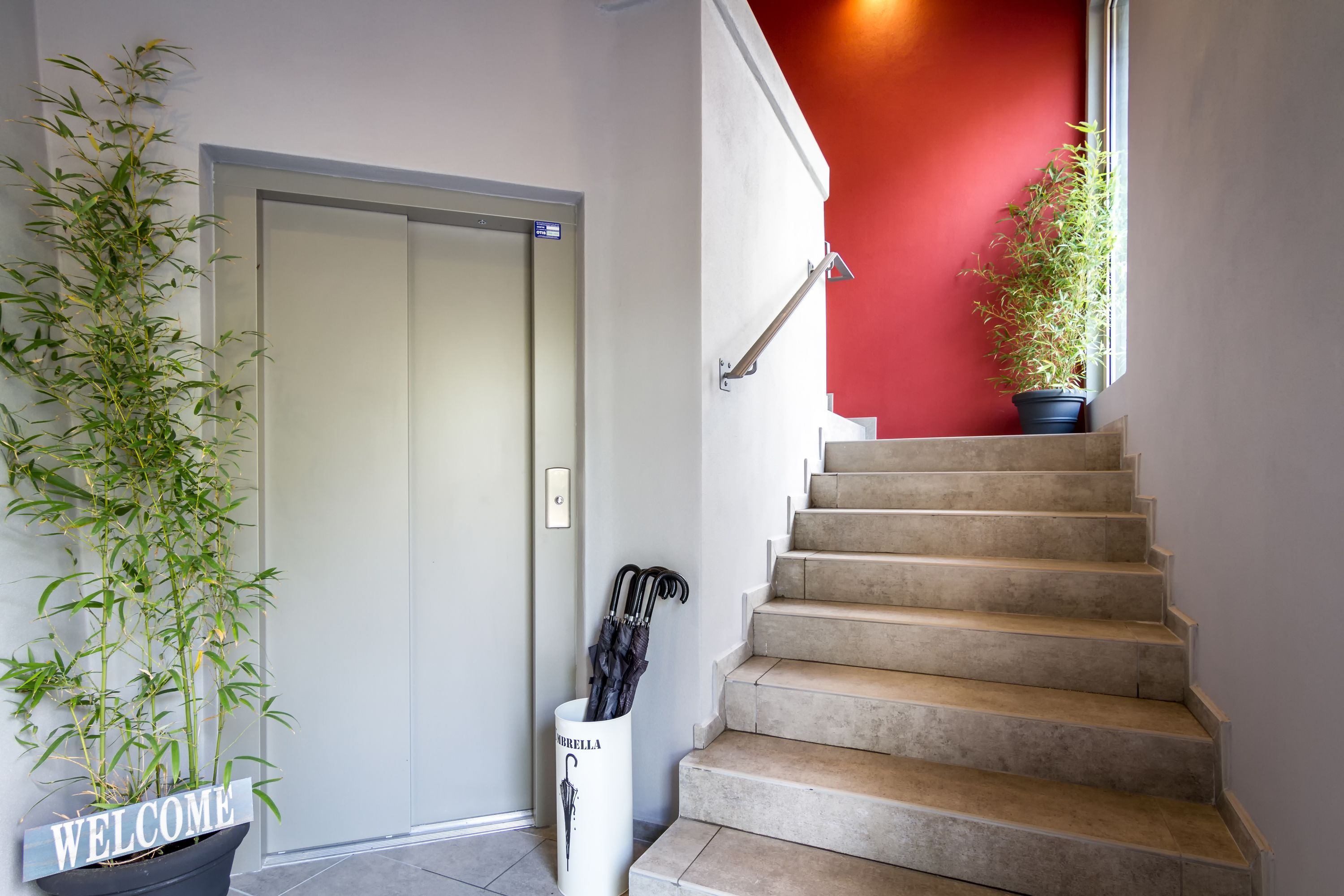 A staircase with a red wall above it, a welcome sign, and a potted plant.