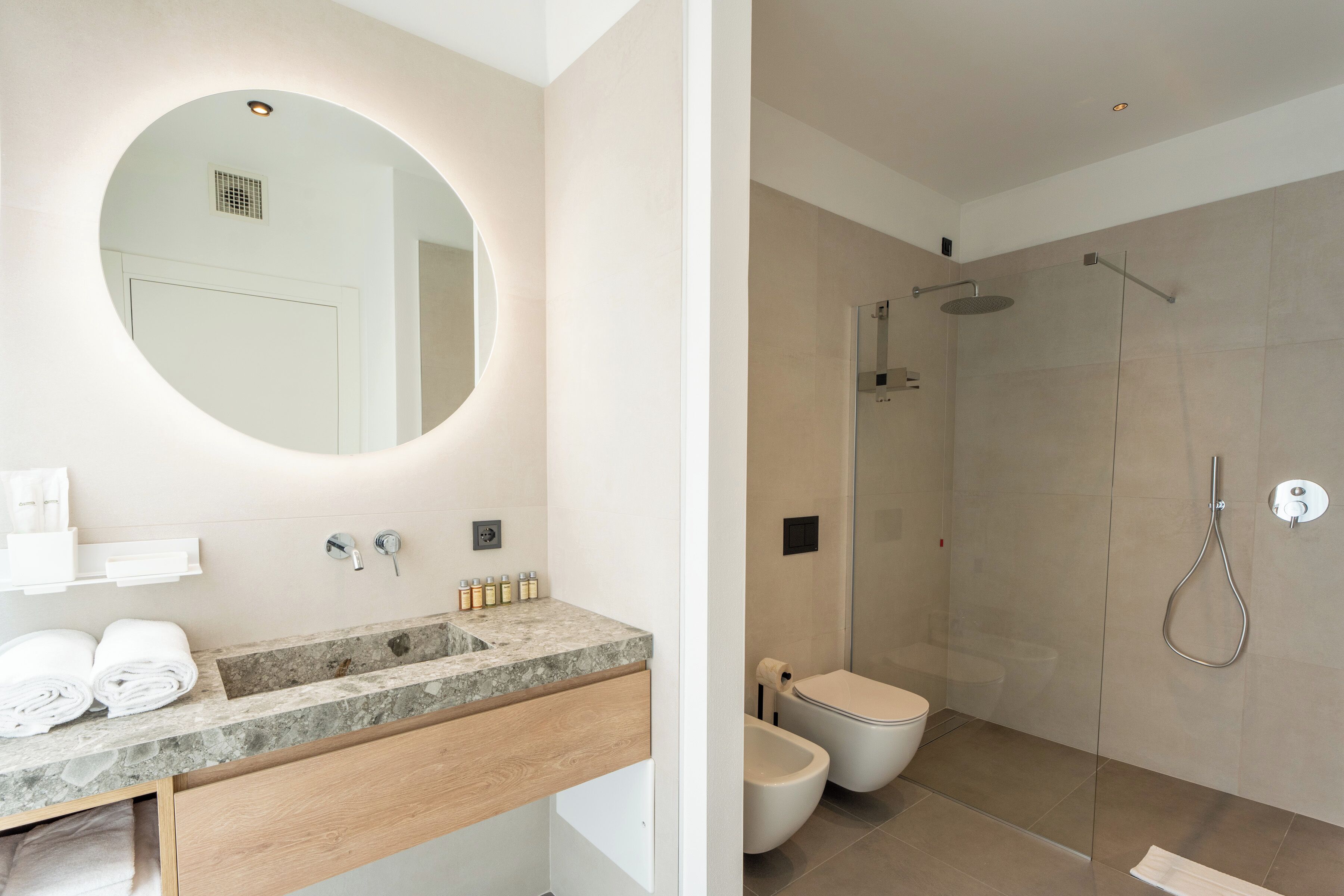 Ein modernes Badezimmer mit rundem Spiegel, Marmorwaschbecken, Toilette und einer Duschkabine.