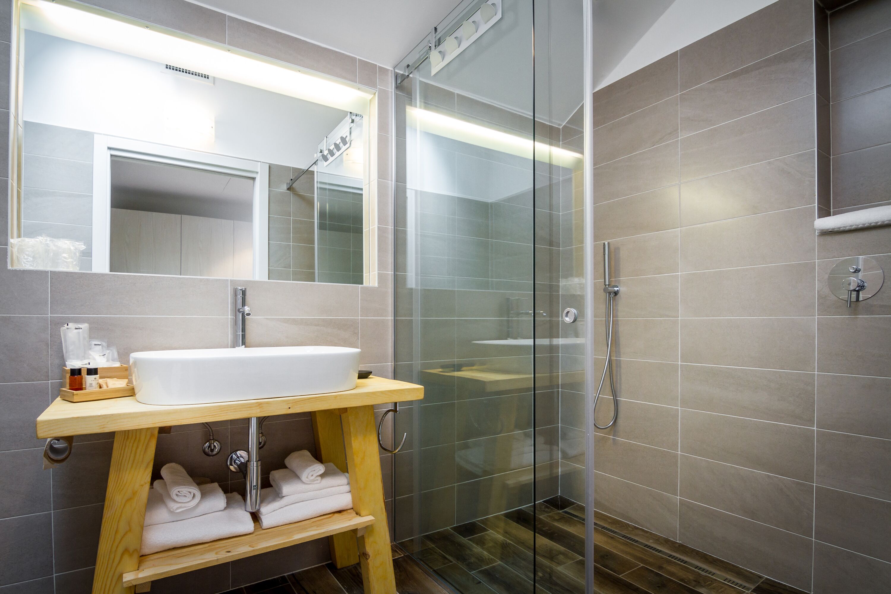 Une salle de bain moderne avec une douche à parois de verre, un meuble-lavabo en bois et des serviettes soigneusement pliées.