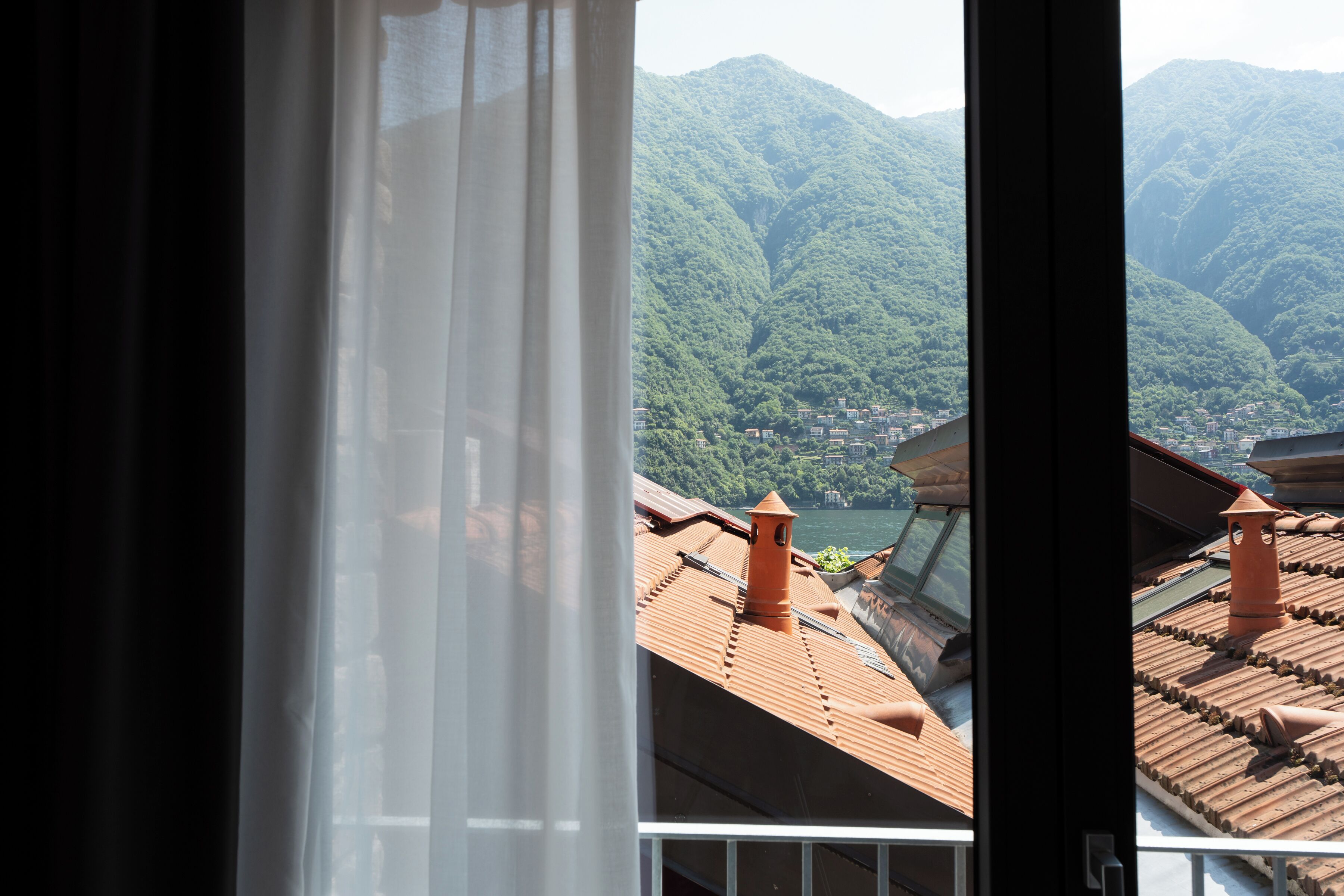 A view through a window with a curtain, revealing a mountain landscape with buildings.