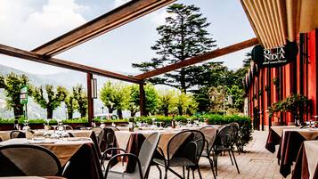 An outdoor restaurant with tables set for dining, surrounded by greenery and mountains in the background.